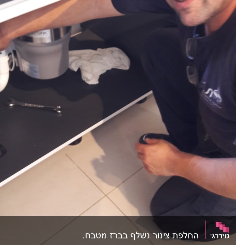 אדם מתקן צנרת מתחת לכיור עם מפתח ברגים
